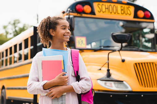 happy student standing in front of a school bus