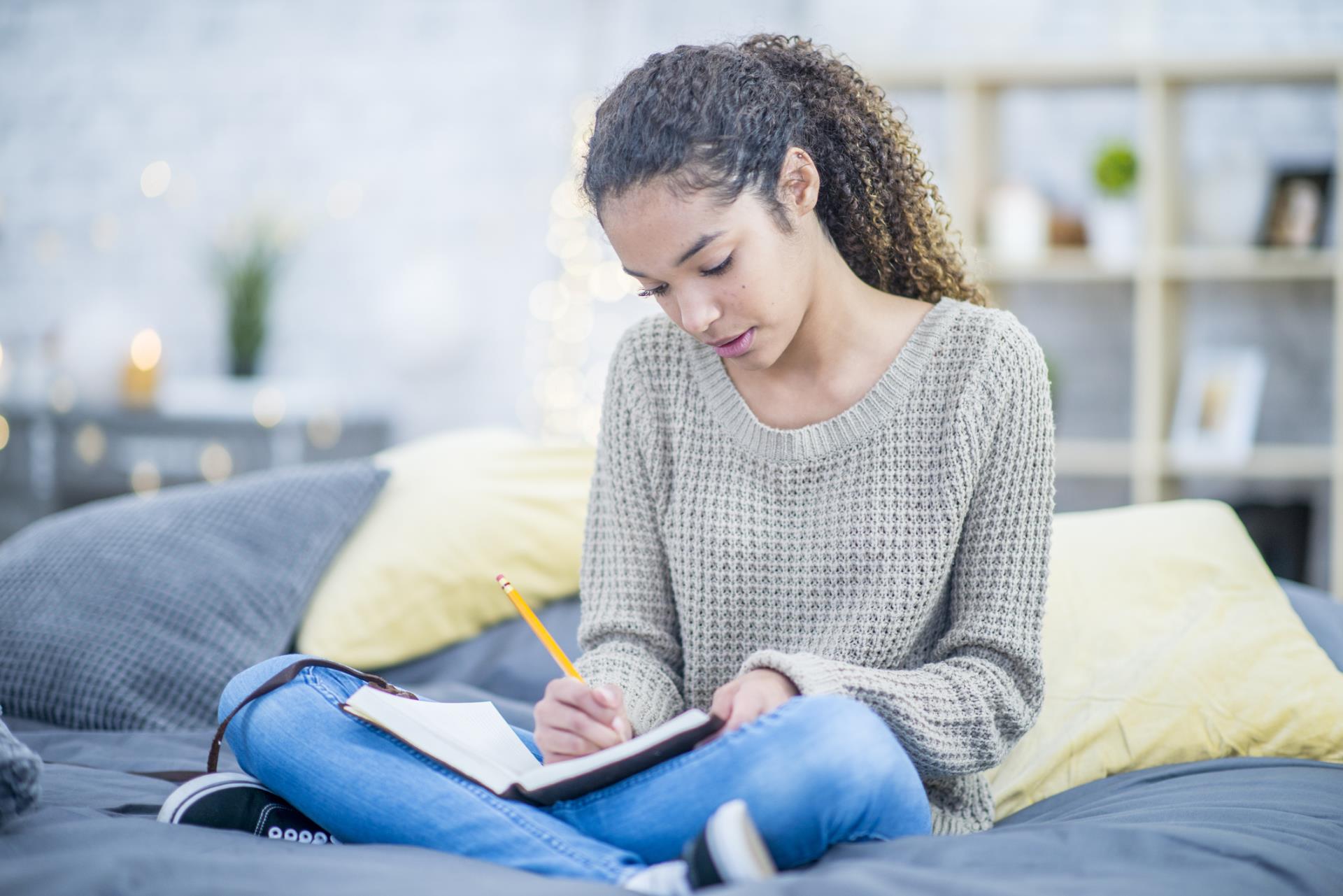 High school student working at home while sitting on their bed.