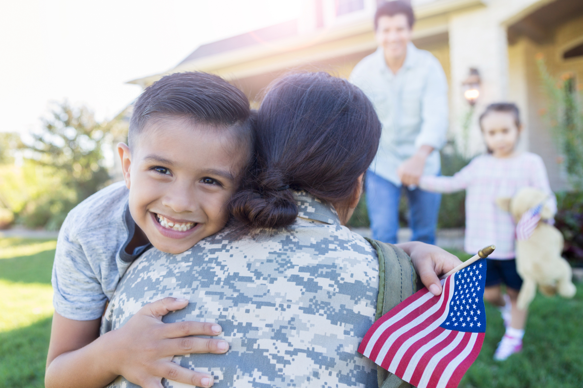 Service member returning home and being greeted by family members with a hug.