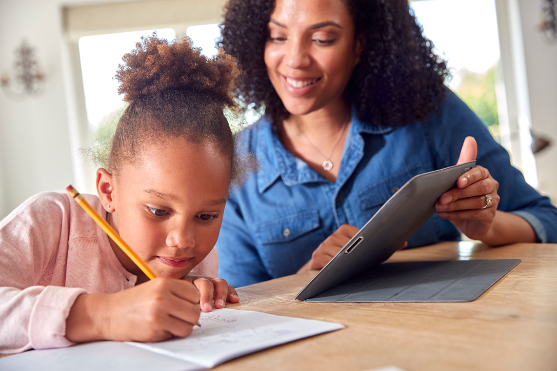 Parent sitting with their child at the dinner table while they do homework.