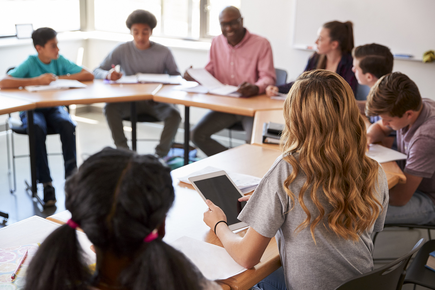 Middle school teacher leading a group discussion with students seated at desks in a circle.