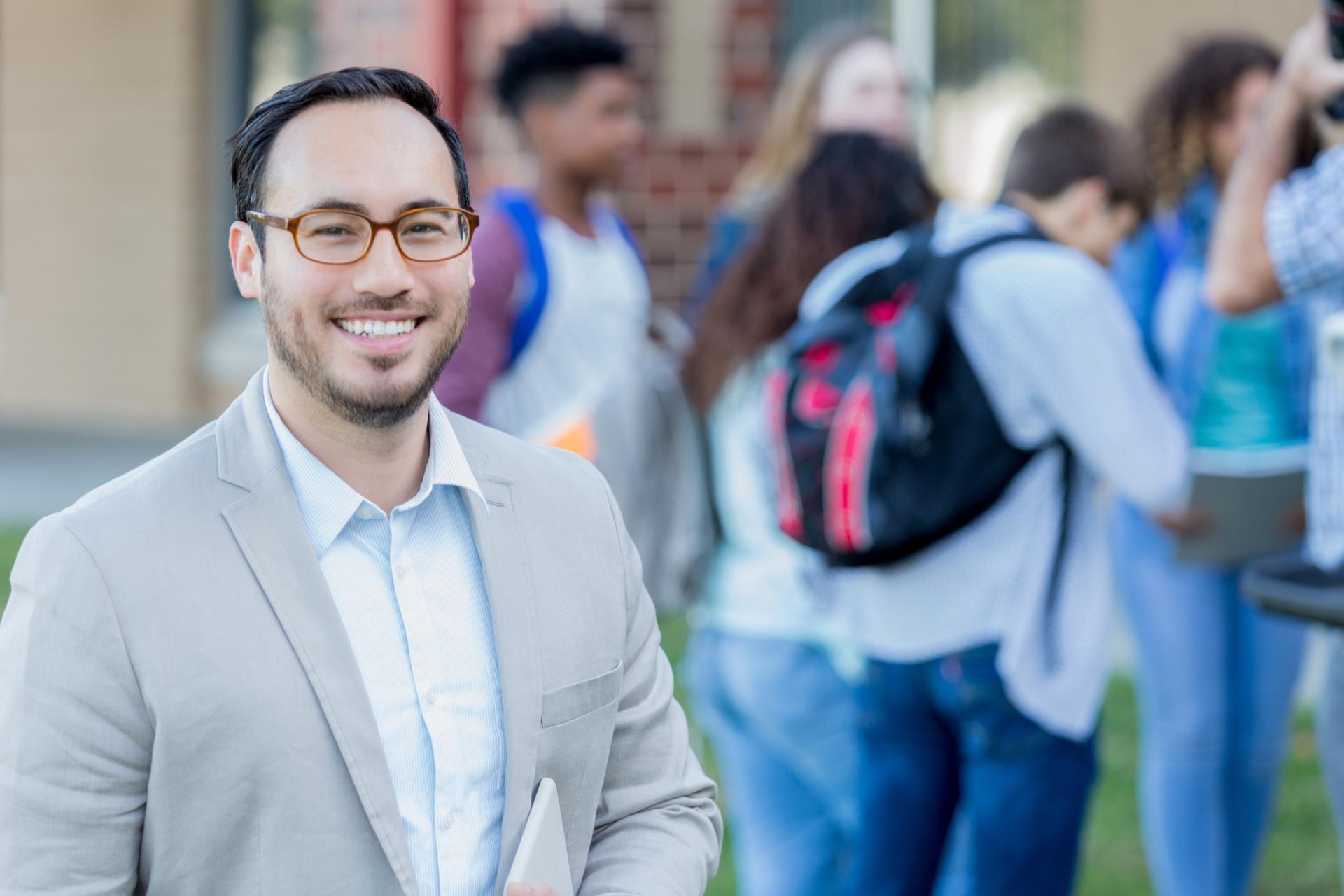 Confident principal standing outside of school while students arrive at school.