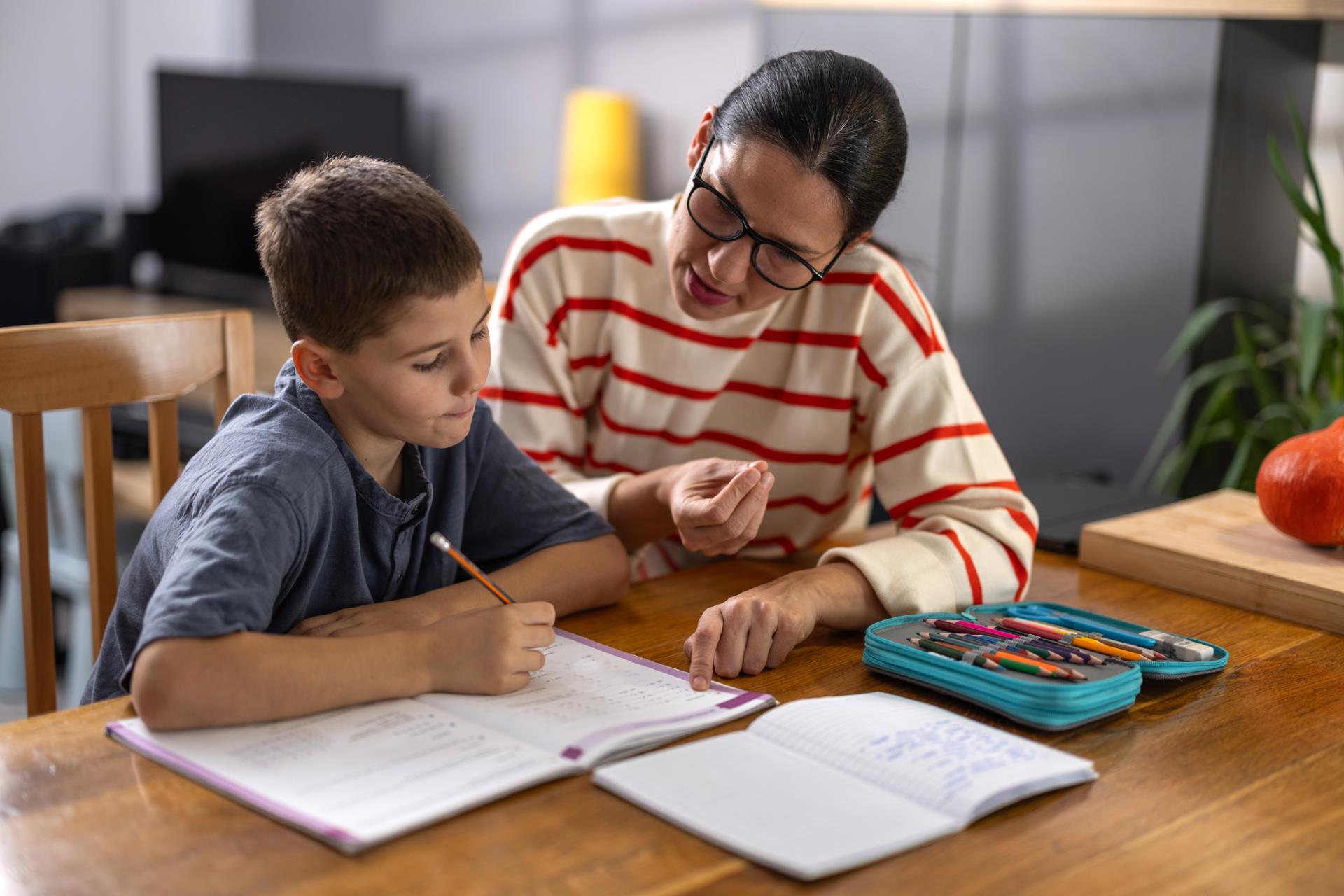 Parent helps child with homework at the dinner table.