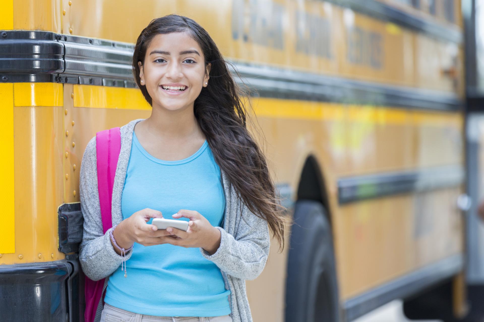 Middle school student waiting for school bus while on their phone.